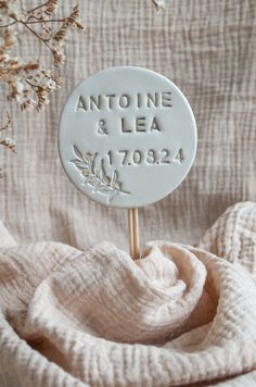 a close up of a white sign on a wooden stick with flowers in the background