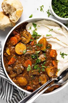 a bowl filled with stew, mashed potatoes and carrots next to some bread