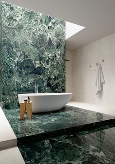 a bath tub sitting next to a white sink in a room with green marble walls