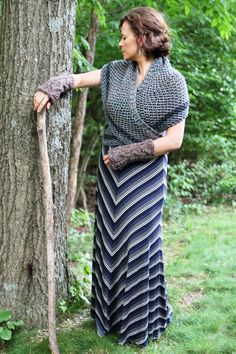 a woman leaning against a tree with her arm wrapped around the tree trunk and wearing gloves