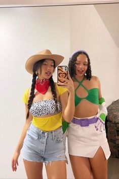 two women in short shorts and hats taking a selfie with a cell phone while standing next to each other