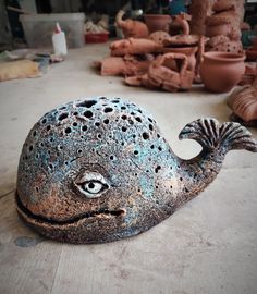 a close up of a fish shaped object on a wooden floor with clay pots in the background