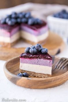 a piece of cheesecake with blueberries on top is sitting on a wooden plate