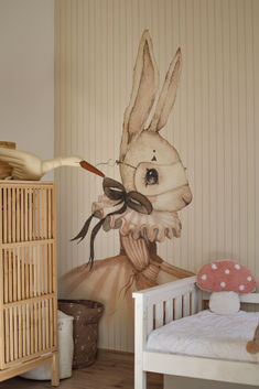 a child's room with a bed, dresser and wallpaper featuring a painting of a rabbit