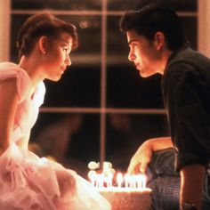 a man and woman sitting next to each other in front of a cake with candles on it