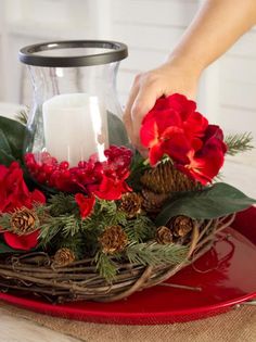 a candle is lit in a glass vase with red flowers and greenery on a tray