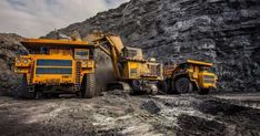 two dump trucks are parked in front of a mountain