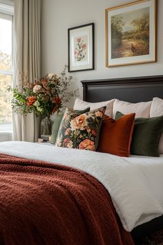 a bed with orange and green pillows in a bedroom next to two pictures on the wall