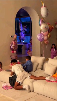 a group of children sitting on top of a white couch in a living room next to balloons