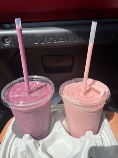 two smoothies with straws are sitting on a tray in the back of a car