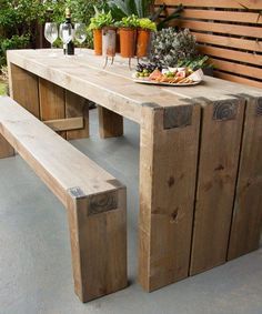 a wooden bench sitting on top of a cement floor next to a table filled with vegetables