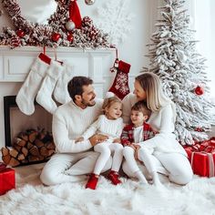 a man, woman and child sitting in front of a christmas tree with stockings on it