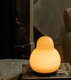 a lamp sitting on top of a table next to a book and glass vase in front of it