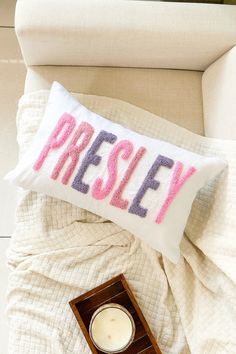 a pillow that says presly on it next to a candle