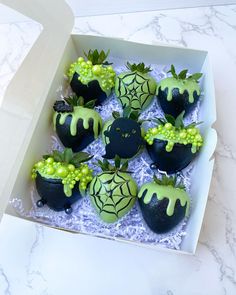 a box filled with green and black decorated strawberries