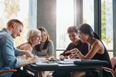 a group of people sitting around a table with notebooks and pens in their hands