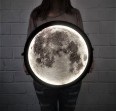 a woman holding a large illuminated moon in front of her face