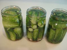 three jars filled with pickles sitting on top of a table