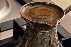 a metal pitcher sitting on top of a stove next to a burner with a spoon in it