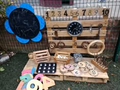 an assortment of wooden items on display in front of a fence with numbers and clocks