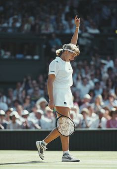 a tennis player waves to the crowd as she walks across the court with her racket