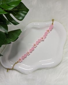 a pink beaded necklace sitting on top of a white tray next to a plant