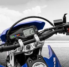 a close up of the handlebars on a blue and black motorcycle with mountains in the background