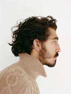 a man with long hair and a goatee looks off into the distance while wearing a turtle neck sweater