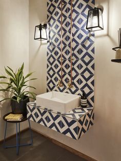 a bathroom with a sink, mirror and plant in it next to a tiled wall