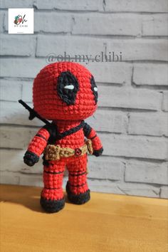 a crocheted deadpool doll is sitting on a table with a brick wall in the background