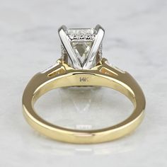 a yellow and white gold engagement ring with a princess cut diamond on the side, sitting on a marble surface