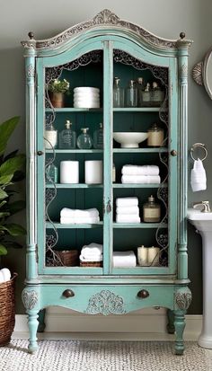 a blue china cabinet with lots of white dishes on top and towels in the bottom