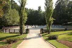 an empty path leading to a horse stable in the middle of some trees and grass