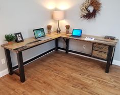 a desk with two laptops on it in a room next to a lamp and pictures