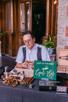 a man sitting at a table with cigars and other items on display in front of him