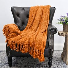 an orange throw blanket sitting on top of a chair next to a potted plant