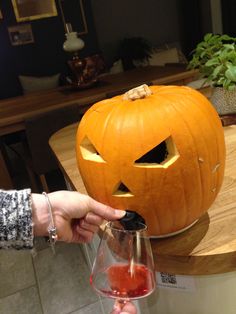 a person holding a wine glass in front of a carved pumpkin