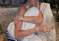 a woman sitting on the ground holding a wine glass in her right hand and tattoos on her left arm