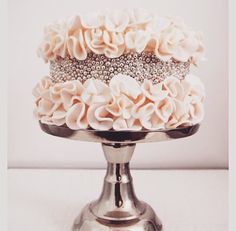 a three tiered cake decorated with flowers on a silver stand in front of a white wall