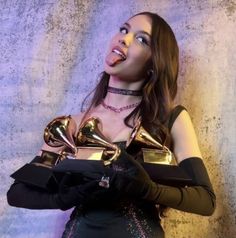 a woman holding three awards in her hands and looking up at the sky while wearing black gloves