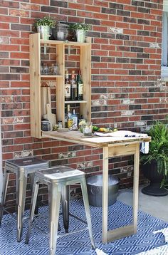 a table and two stools in front of a brick wall with potted plants