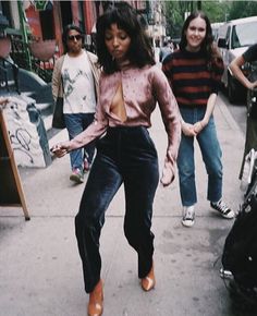 a woman is dancing on the sidewalk with other people behind her and another person walking down the street