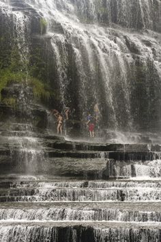 several people are standing in front of a waterfall with water cascading over them