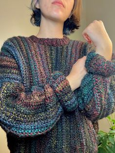 a woman wearing a multicolored sweater and holding her hands on her chest with one hand