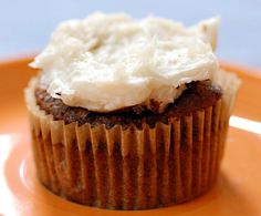 a cupcake with white frosting on an orange plate