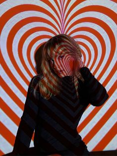 a woman with long blonde hair sitting in front of an orange and white striped background