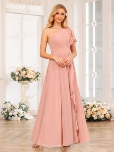 a woman in a long pink dress standing on a wooden floor with flowers behind her