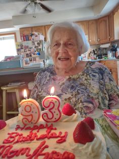 an older woman sitting in front of a birthday cake with two candles on top of it