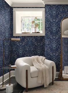 a white chair sitting in front of a window next to a wall covered in blue flowers