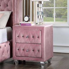 a pink bed and nightstand with a clock on the night stand in front of it